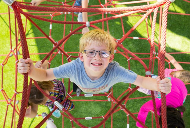 Little boy playing on Lunar Blast Shade Climber at Mt. Ton of Fun featuring Playground Grass by ForeverLawn