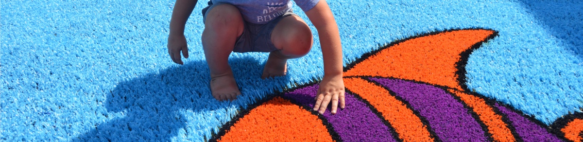 Little boy looking at fish Funsert on playground created with Playground Grass synthetic turf