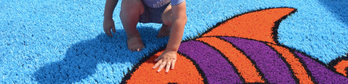 Little boy touching fish Funsert on Playground Grass synthetic turf by ForeverLawn